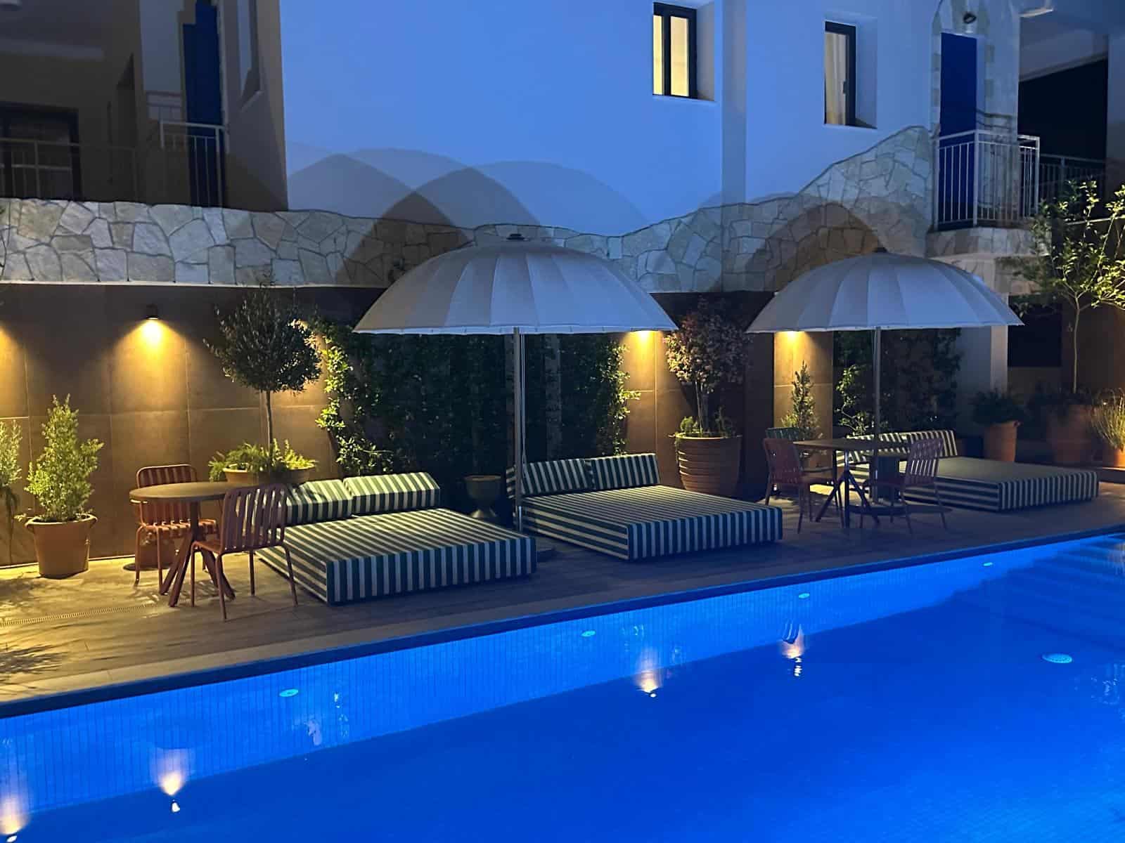 מיטות שמש מפוספסות ושמשיות לצד הבריכה המוארת בערב
